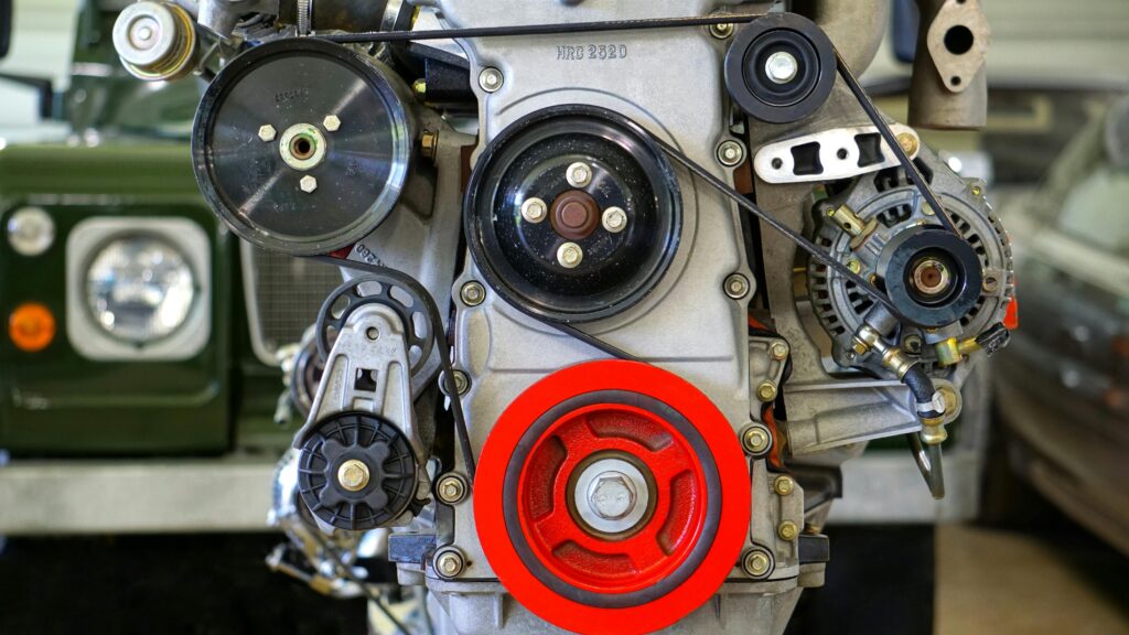 Detailed view of a car engine showcasing belts and colorful pulleys in a workshop setting.